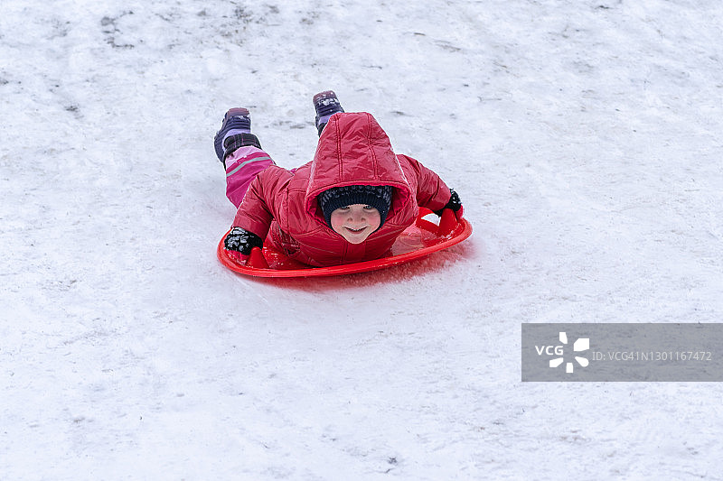 一个小女孩骑着雪橇从冬季滑梯上滑下来图片素材