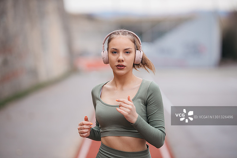 一个漂亮的女人在跑道上跑步，戴着耳机听音乐图片素材