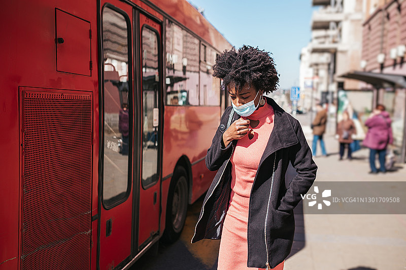 优雅的女商人戴着防护面具，独自站在空旷的街道上等待公共汽车或出租车。冠状病毒或Covid-19生活方式概念。图片素材