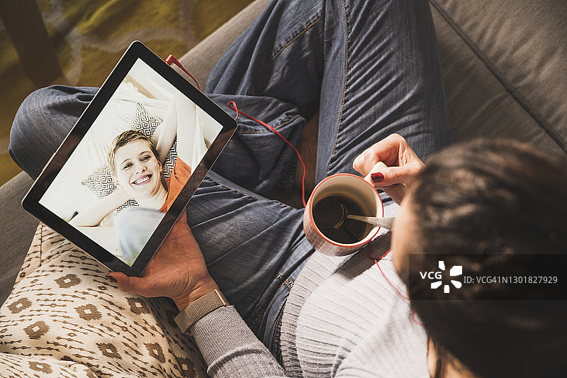 成熟的女人拿着咖啡杯，在家里的数字平板电脑上视频通话图片素材