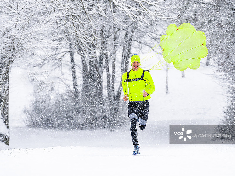 一个年轻人带着降落伞在冬天的森林里的雪地上奔跑图片素材