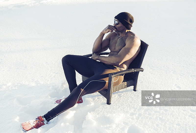 当坐在雪地里的椅子上时，沉思的赤胸运动员望向别处图片素材