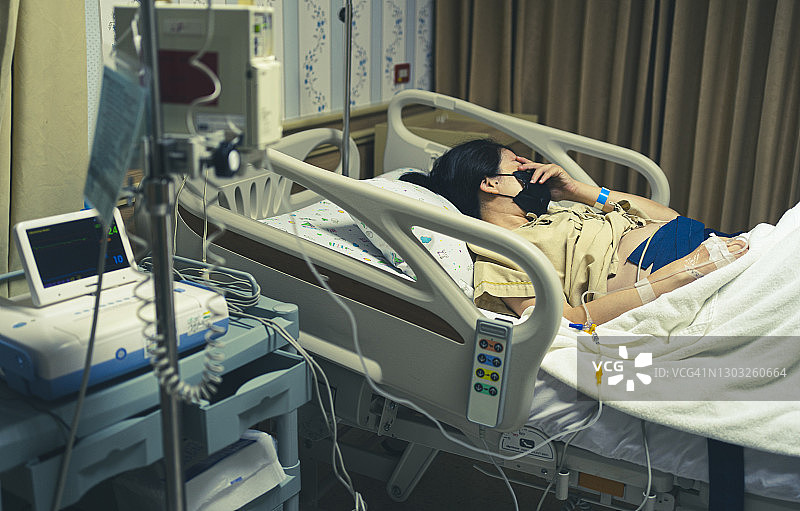 亚洲母亲睡在床上，在分娩前用心率带监测器检查婴儿的脉搏图片素材