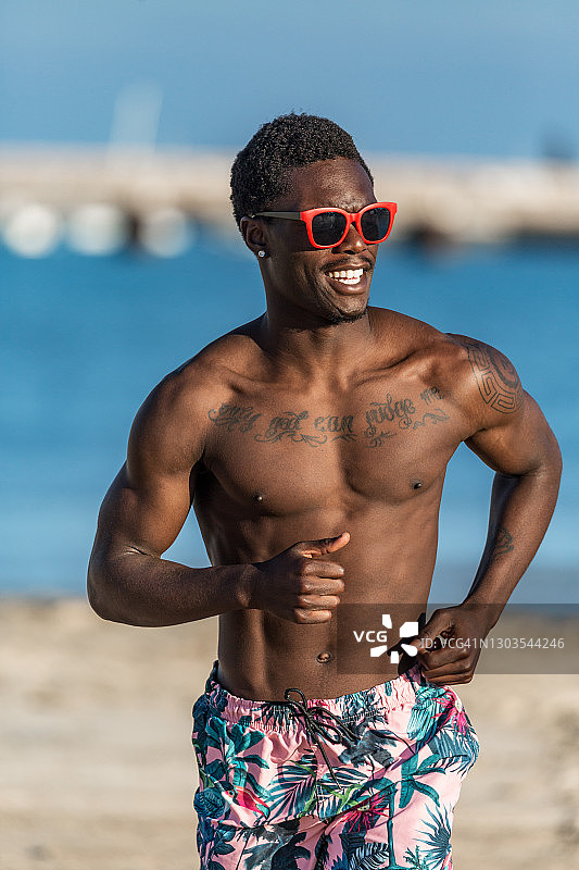 时髦的赤膊黑男人戴着墨镜在海边跑步图片素材
