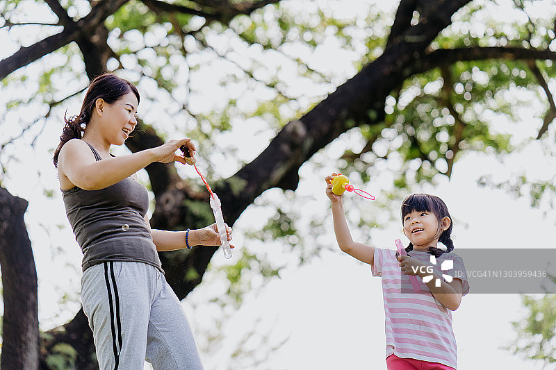 亚洲华人母亲和女儿在公园吹泡泡图片素材