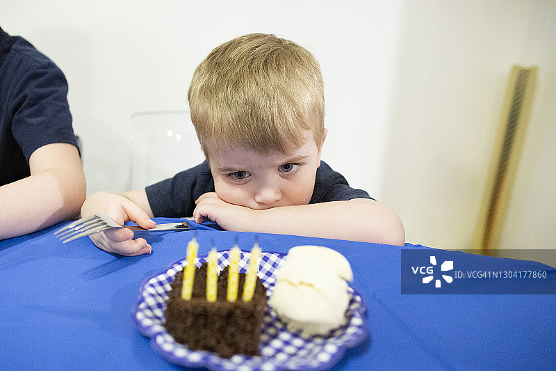 孩子坐在桌子前盯着蛋糕里的生日蜡烛图片素材