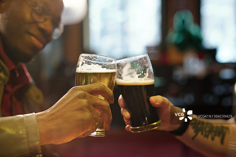 酒吧里两个年轻的跨文化男子的手碰杯图片素材