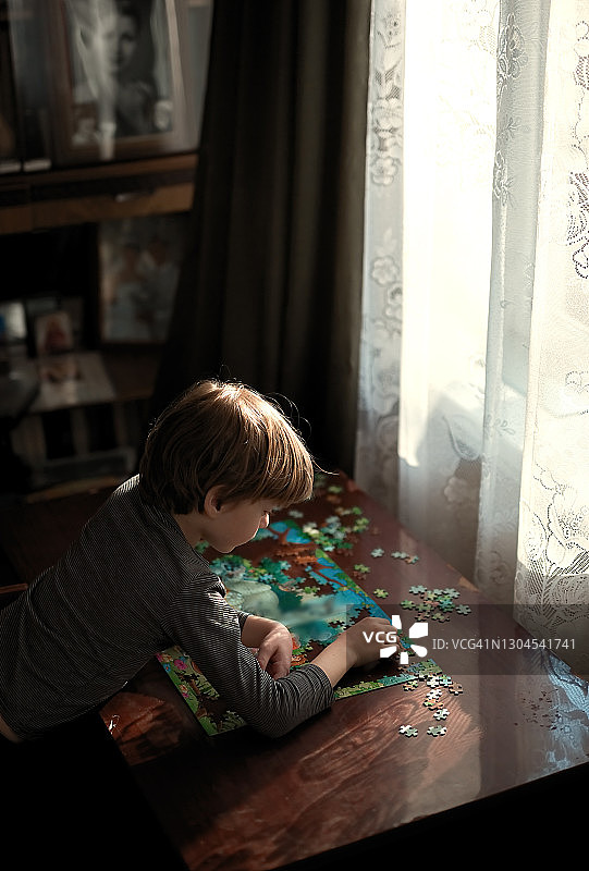 那男孩收集桌上的字谜。自然光线。图片素材