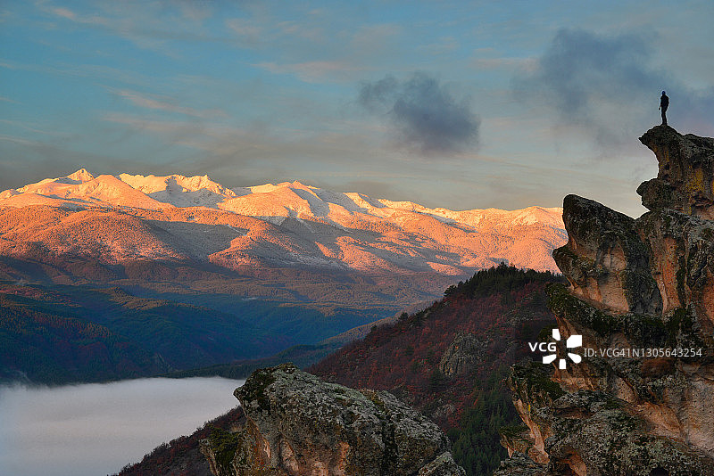 一个人站在岩石上看日出的雪山图片素材