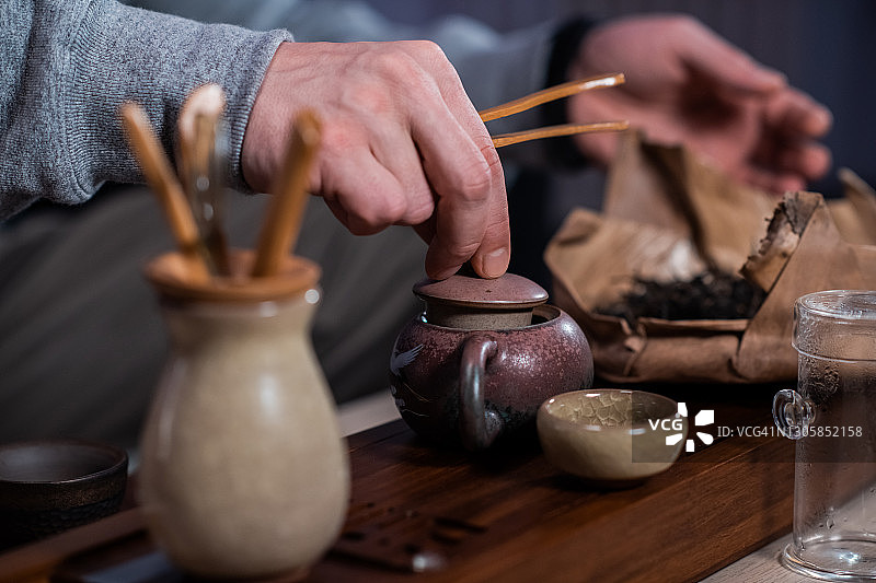 男子双手将特制的竹夹茶叶放入宜兴托盘制成的陶瓷茶壶中。制作中国茶的过程图片素材