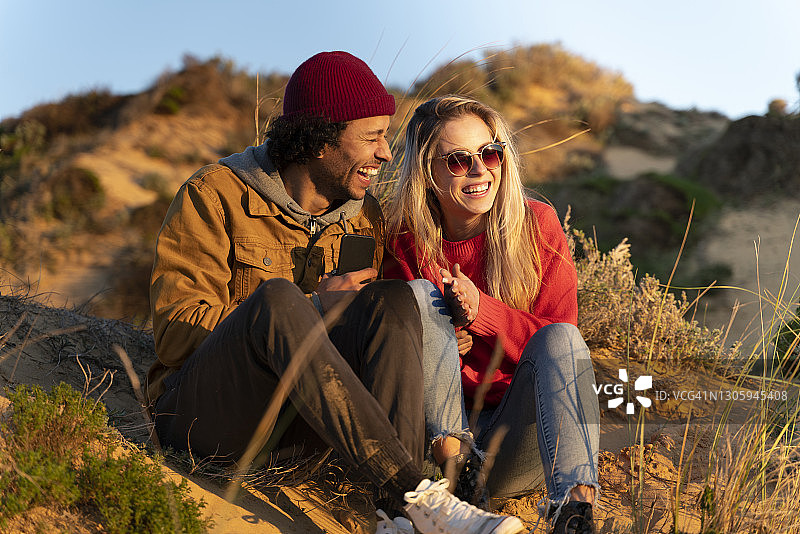 女朋友微笑，而坐在愉快的男朋友在沙丘日落图片素材