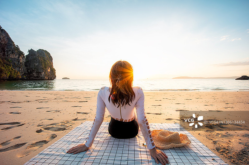 在泰国甲米的拉伊雷海滩，年轻女子坐在日落时的海滩上望向大海图片素材