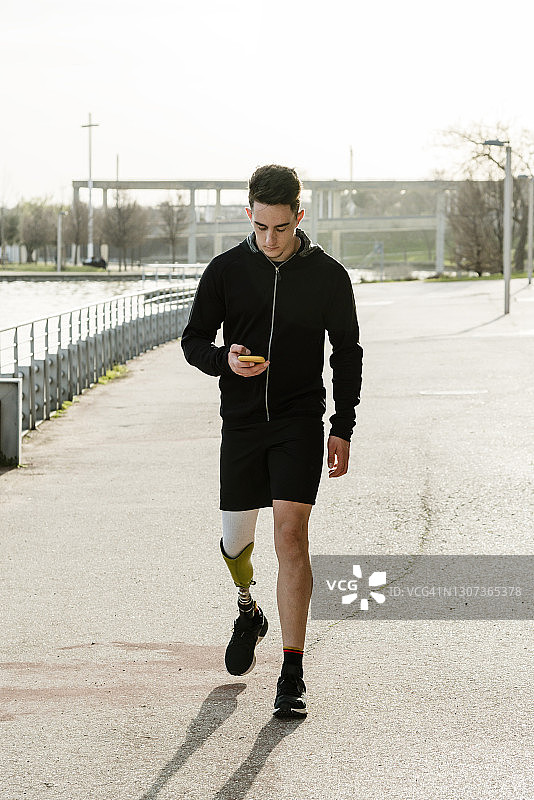 一名戴假肢的男子在街头健身前浏览智能手机图片素材