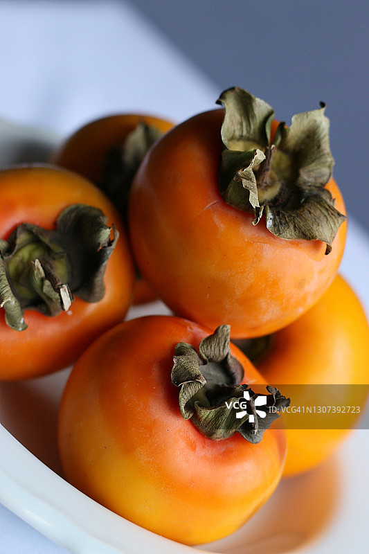 新鲜成熟的柿子在白色经典设计盘子，天堂棕榈树图片素材
