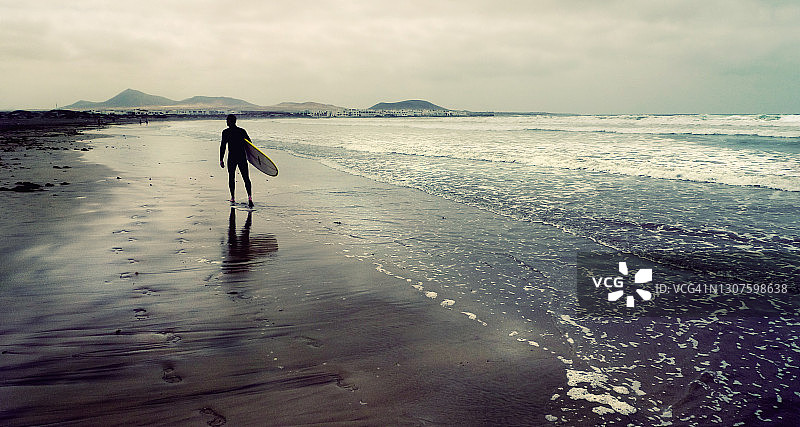 一个孤独的冲浪者沿着空荡荡的海滩行走图片素材