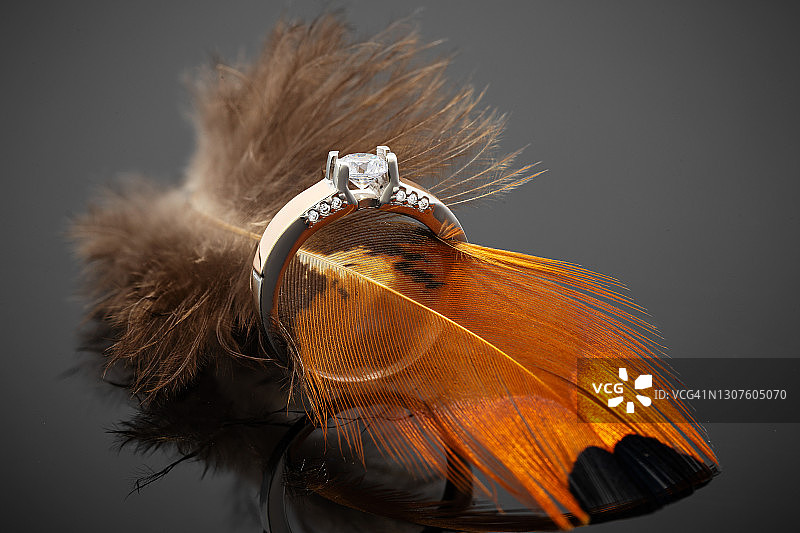 黄金订婚戒指与钻石在黑色背景和橙色羽毛图片素材