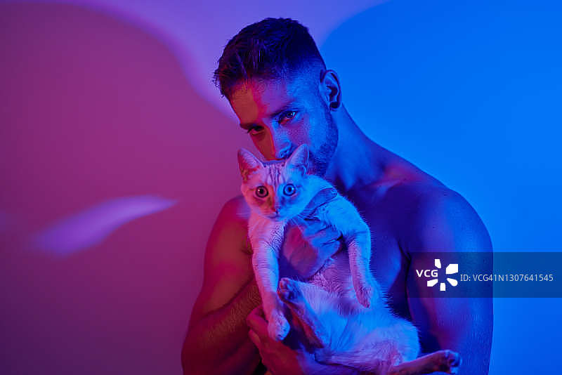 一个男人抱着一只猫，被红蓝相间的霓虹灯照亮。图片素材