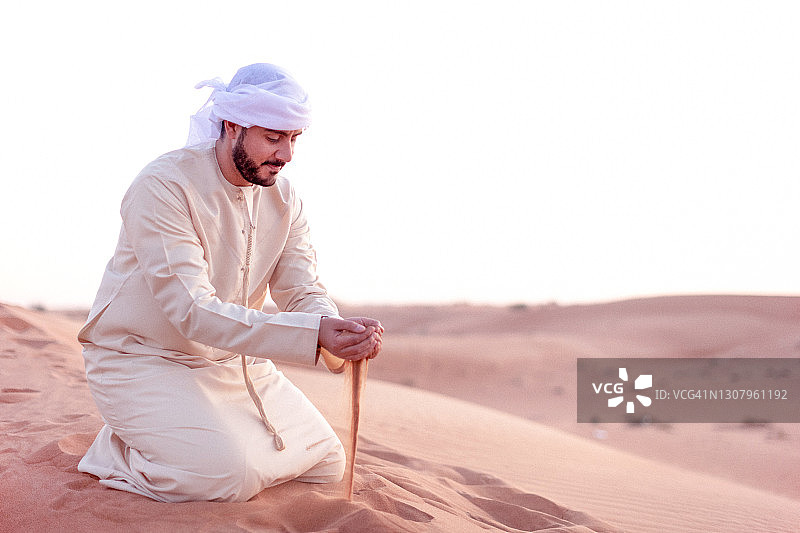 一个阿拉伯人拿着一把沙子站在沙丘上图片素材