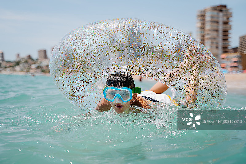 在贝尼多姆，一个快乐的白人孩子戴着护目镜，在夏天享受浮动或内胎沐浴图片素材