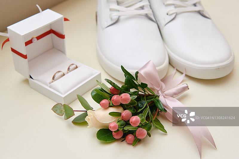 近距离的新郎胸襟与粉色丝带，白色男性鞋和结婚戒指在白色背景，复制空间。现代人配件。婚礼的细节图片素材