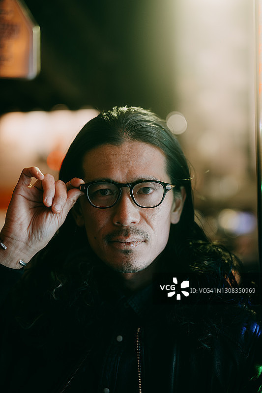 在东京，一名留着长发、戴着眼镜的日本男子在晚上看着照相机图片素材