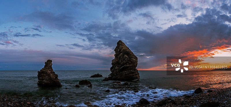 美丽的日落在地中海海滩与岩石从海中浮现。图片素材