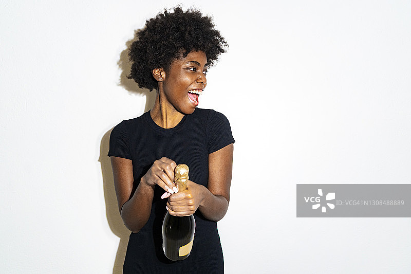 快乐的女人看向别处，同时打开香槟酒瓶站在白色的背景图片素材