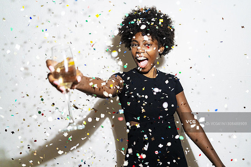 一个兴高采烈的女人拿着香槟笛站在五彩纸屑中，映衬着白色的背景图片素材