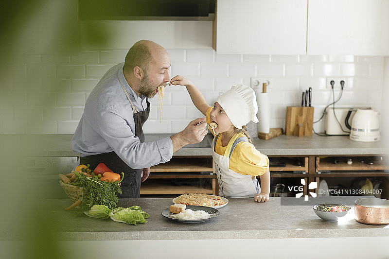 父亲和女儿站在厨房里互相喂面条图片素材