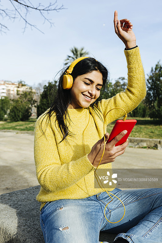 带着耳机微笑的女人在公园里拿着手机跳舞图片素材