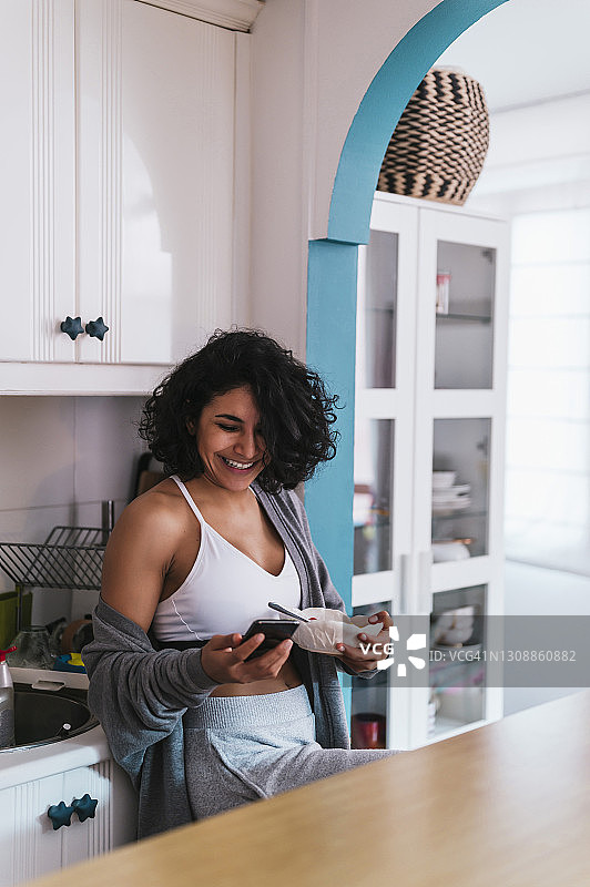 微笑的女人拿着水果盘，而使用智能手机在厨房图片素材