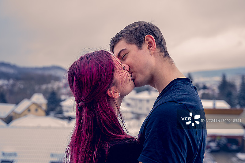 一对年轻夫妇在他们新家的阳台上接吻。背景是雪景。图片素材