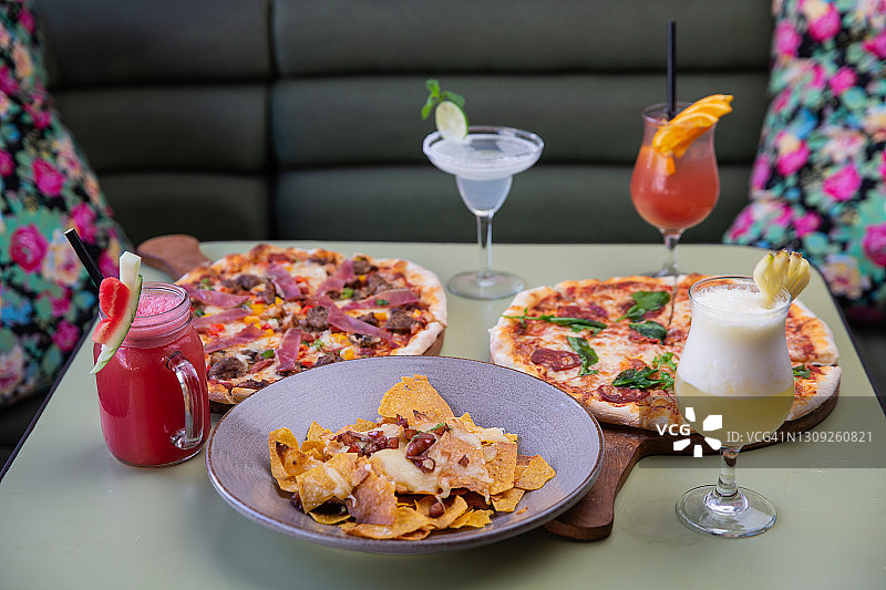 各种美味新鲜的披萨、小吃和饮料供应在餐厅的餐桌上图片素材