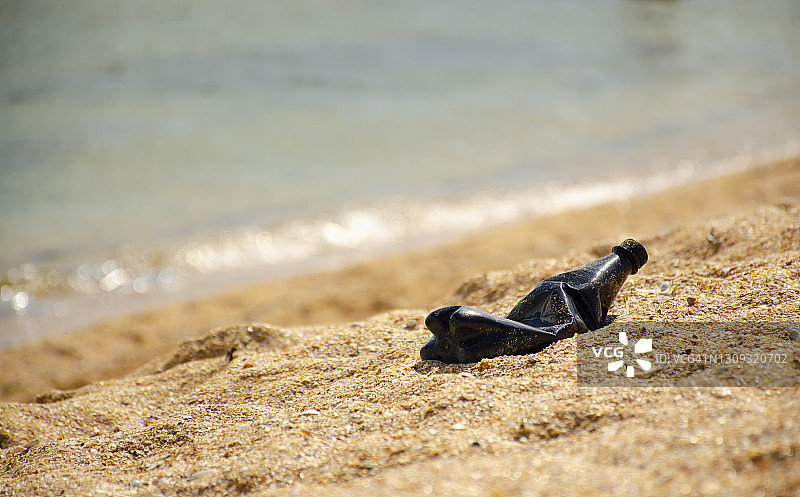 在阳光和大海的背景下，海滩上的黑色塑料瓶或垃圾。环境的概念。图片素材