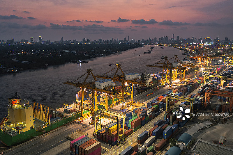 航拍码头商埠的集装箱货仓和集装箱船，以城市景观为背景，经营物流、进出口、航运或货运。图片素材