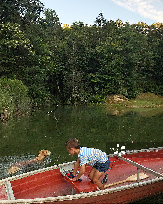 坐在独木舟上的小男孩和他的狗在水里游泳图片素材