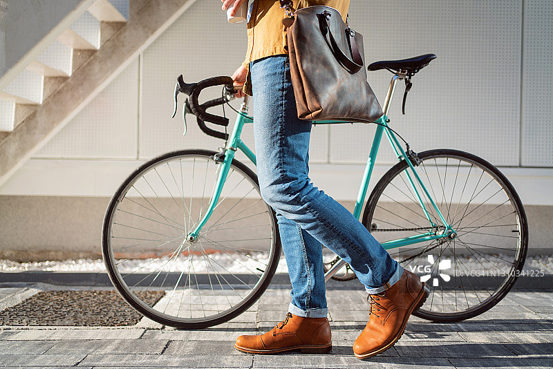 侧面的观点，一个不认识的人走与他的自行车，而携带一杯咖啡图片素材