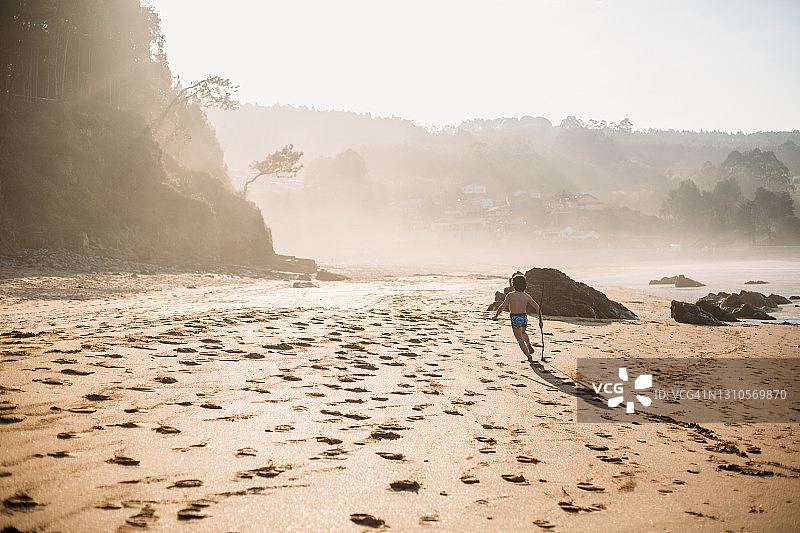日落时分，男孩拄着拐杖在空旷的海滩上奔跑图片素材