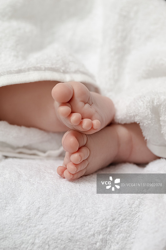 婴儿的想法和概念。一个4周大的男婴在白色毛巾上交叉双脚的微距特写图像。垂直的形象定位图片素材