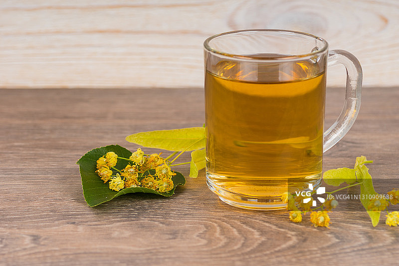 草本茶在透明玻璃杯和新鲜的椴树花在木桌上图片素材