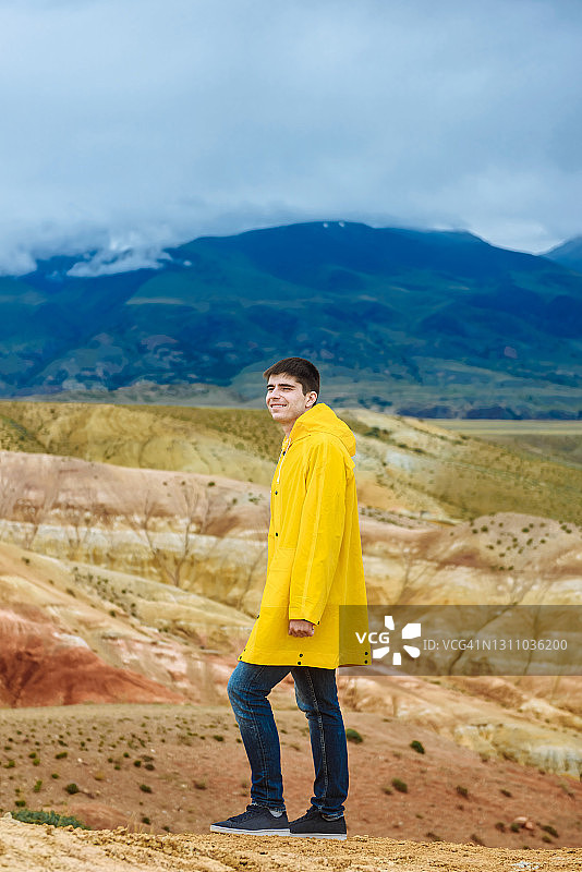 一个穿着黄色库尔特的男人，背景是彩色的山脉。图片素材