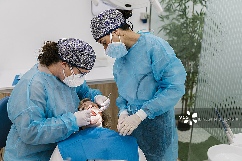 在诊所，牙科矫正医生在助理的陪同下，穿着防护服及面罩检查病人图片素材