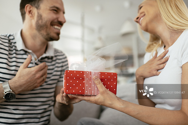 微笑的男人惊喜他的女朋友在家里的礼物。库存图片图片素材