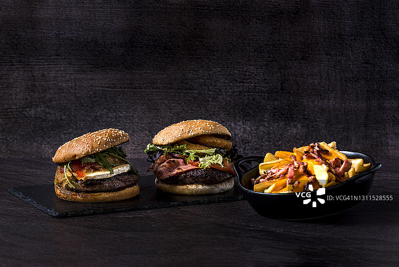 两块有厚奶酪，鱿鱼，生菜，西红柿和薯条的汉堡摆在板上。黑色食品图片素材