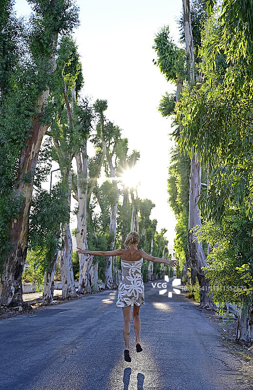 希腊，12月尼斯，哥伦比亚，成年女子在夏天沿着桉树大道快乐地跳跃图片素材