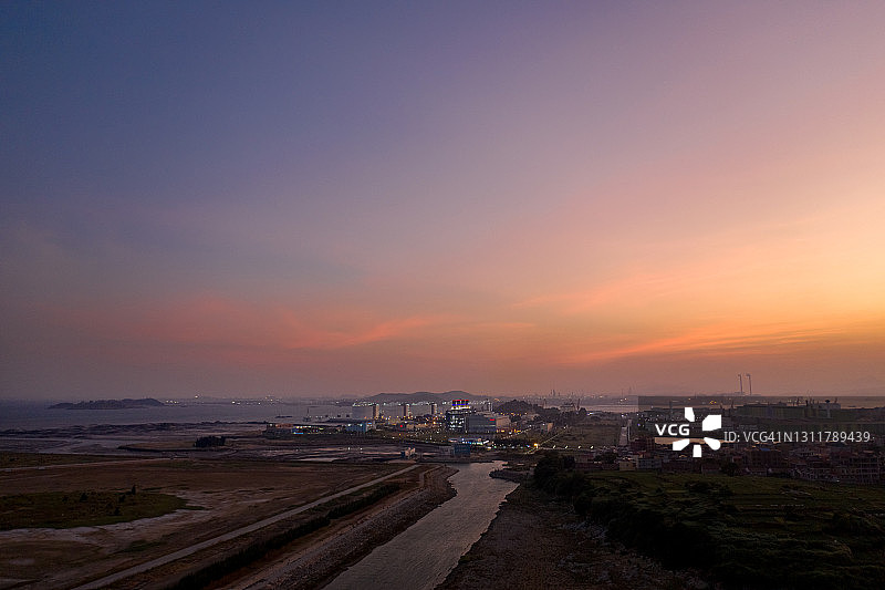 夕阳下空荡荡的海滩，远处是一座化工厂图片素材
