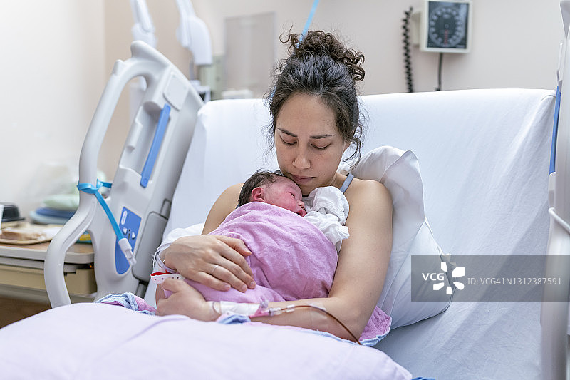 混血母亲在医院病床上对分娩后的新生儿做皮肤对皮肤的结合图片素材