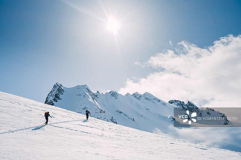 两个滑雪登山运动员在太阳的照耀下爬向山顶图片素材