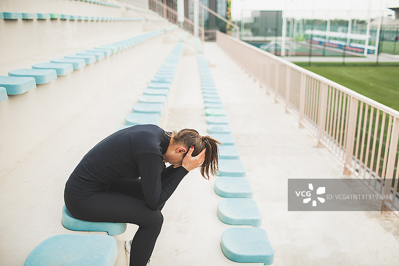疲惫无力的女人在艰苦的跑步训练后坐在体育场的座位上图片素材