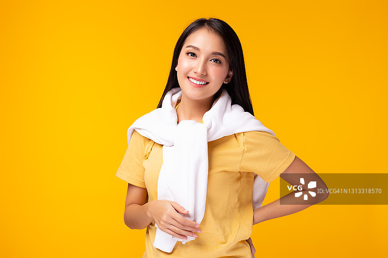 快乐美丽的亚洲女人看着相机友好的微笑表情用一些产品美丽年轻的亚洲女性肖像孤立在黄色的背景好人图片素材
